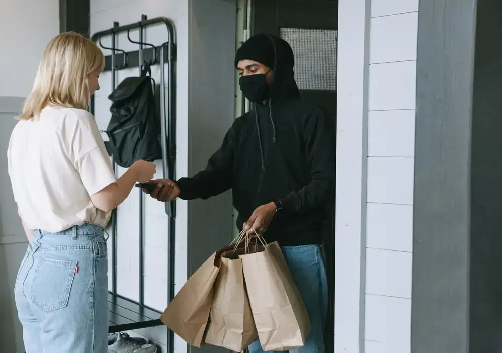 A smiling delivery driver handing over a Crisp and Clean garment bag to a customer at their front door